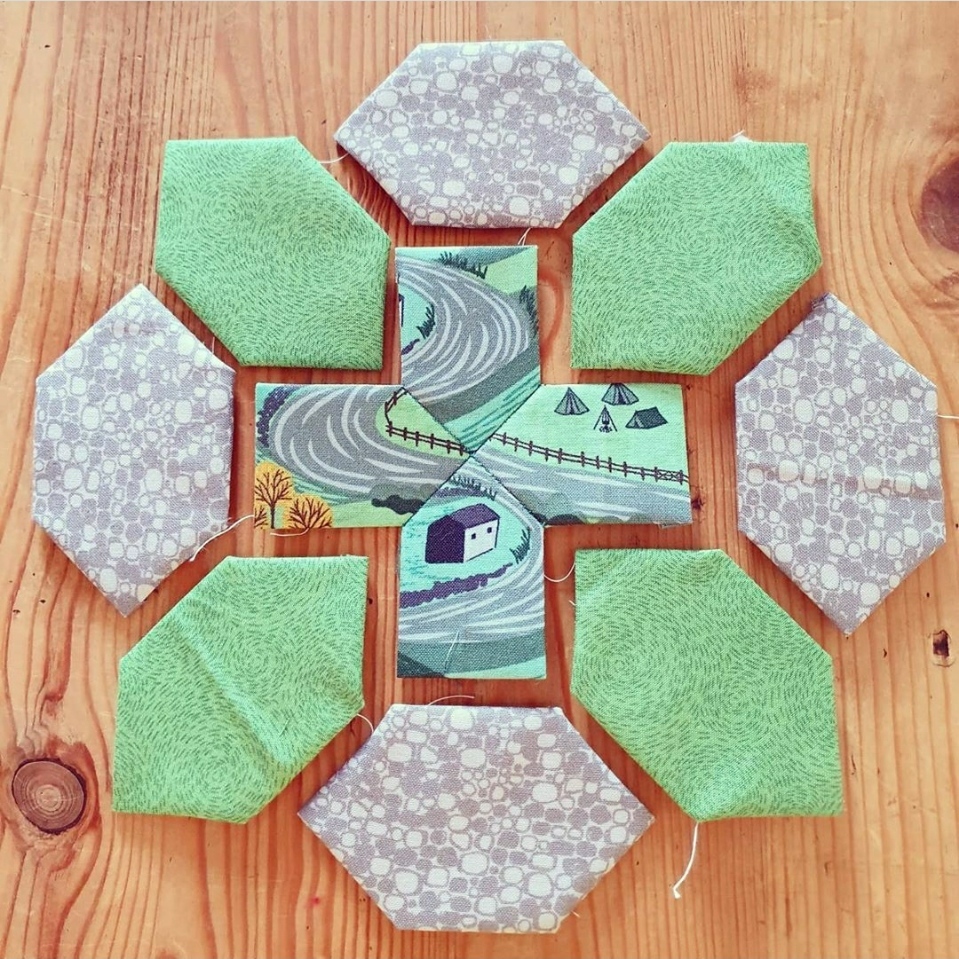 This block is made of a central cross shape made in a fabric of countryside scenes, surrounded by eight honeycomb hexagons, four in green and four in grey.